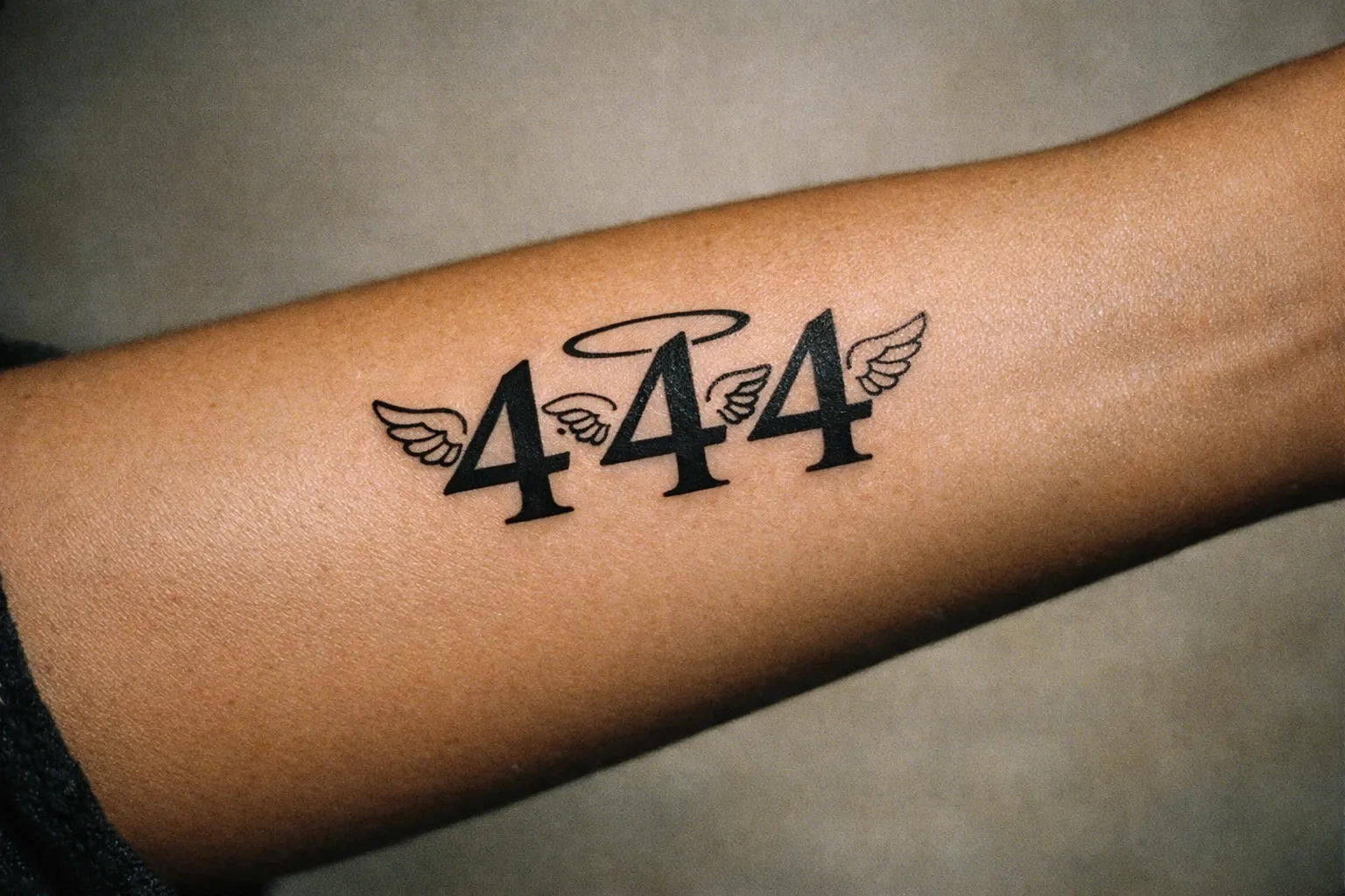 Forearm close-up of a 444 tattoo with a subtle angelic halo integrated into the digits