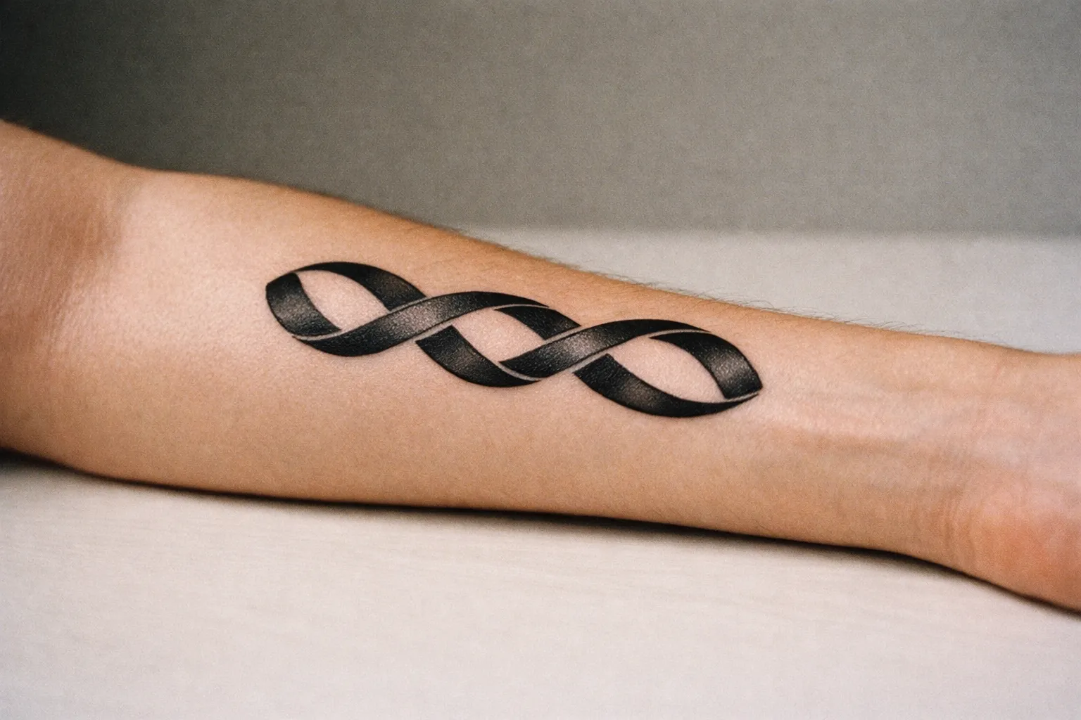 A left inner forearm with three interlocking curved ribbons forming a loop motif, hinting at a 999 concept without digits