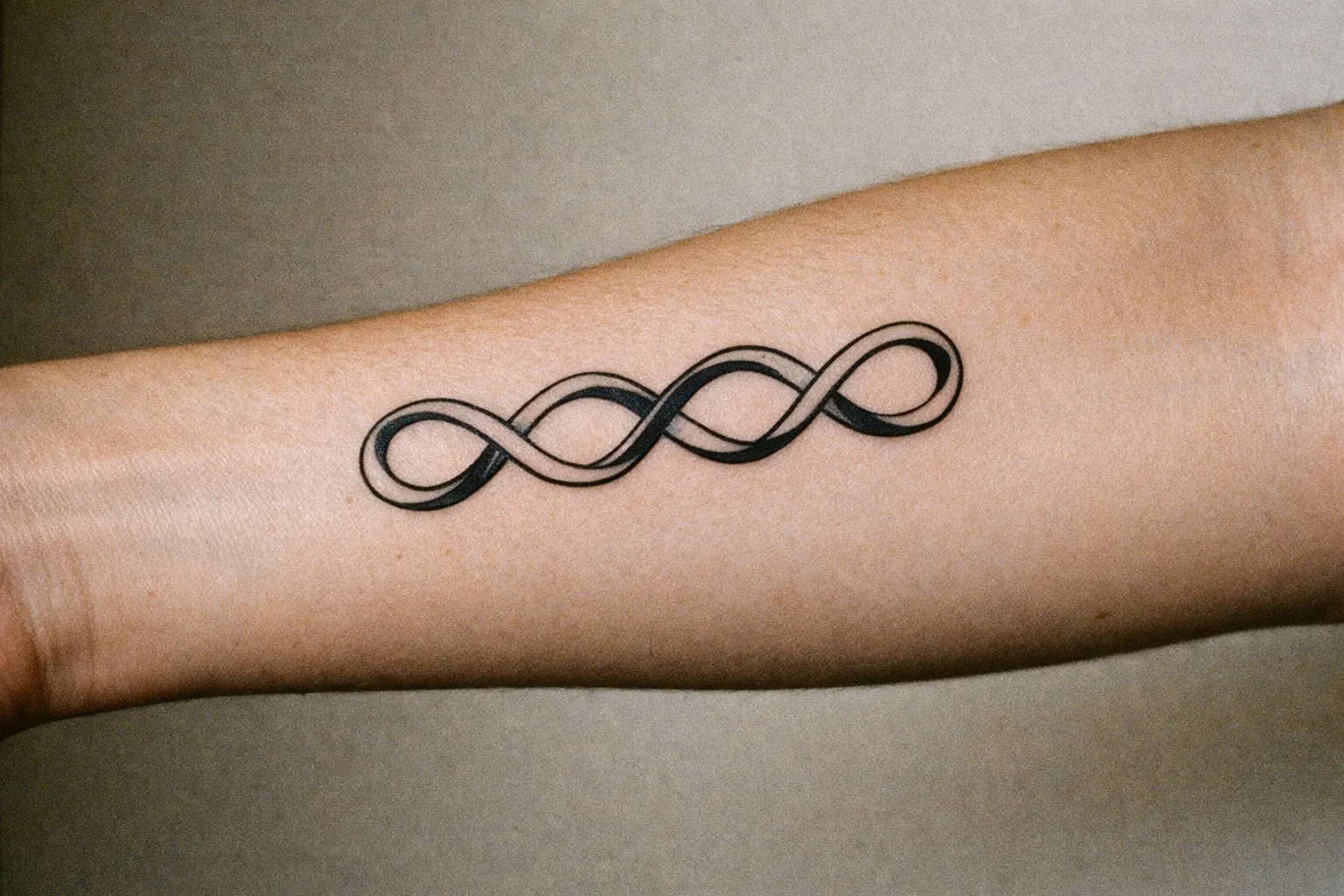 Three interlocking infinity symbols along the inner forearm, suggesting duality without numerals