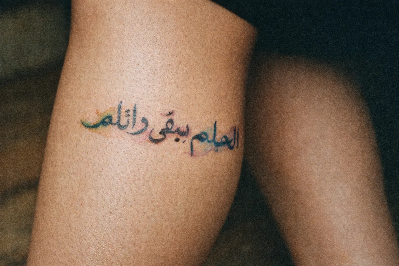 A person's leg displays an Arabic script tattoo with colorful accents.