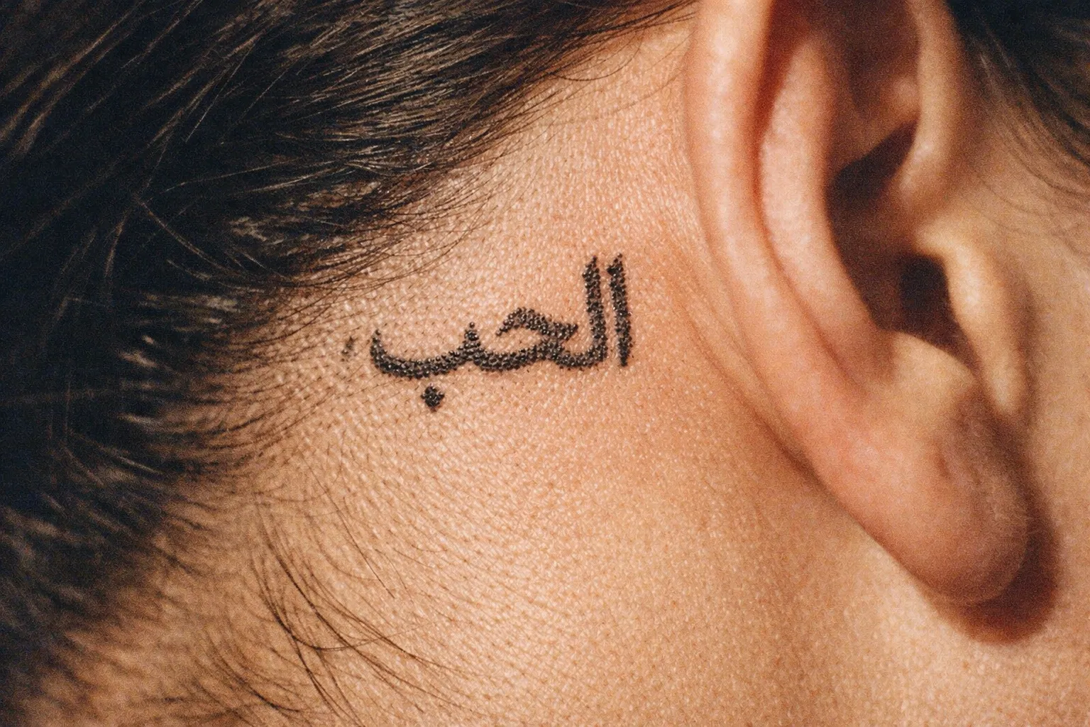 A close-up of a person's neck near the ear with an Arabic script tattoo.