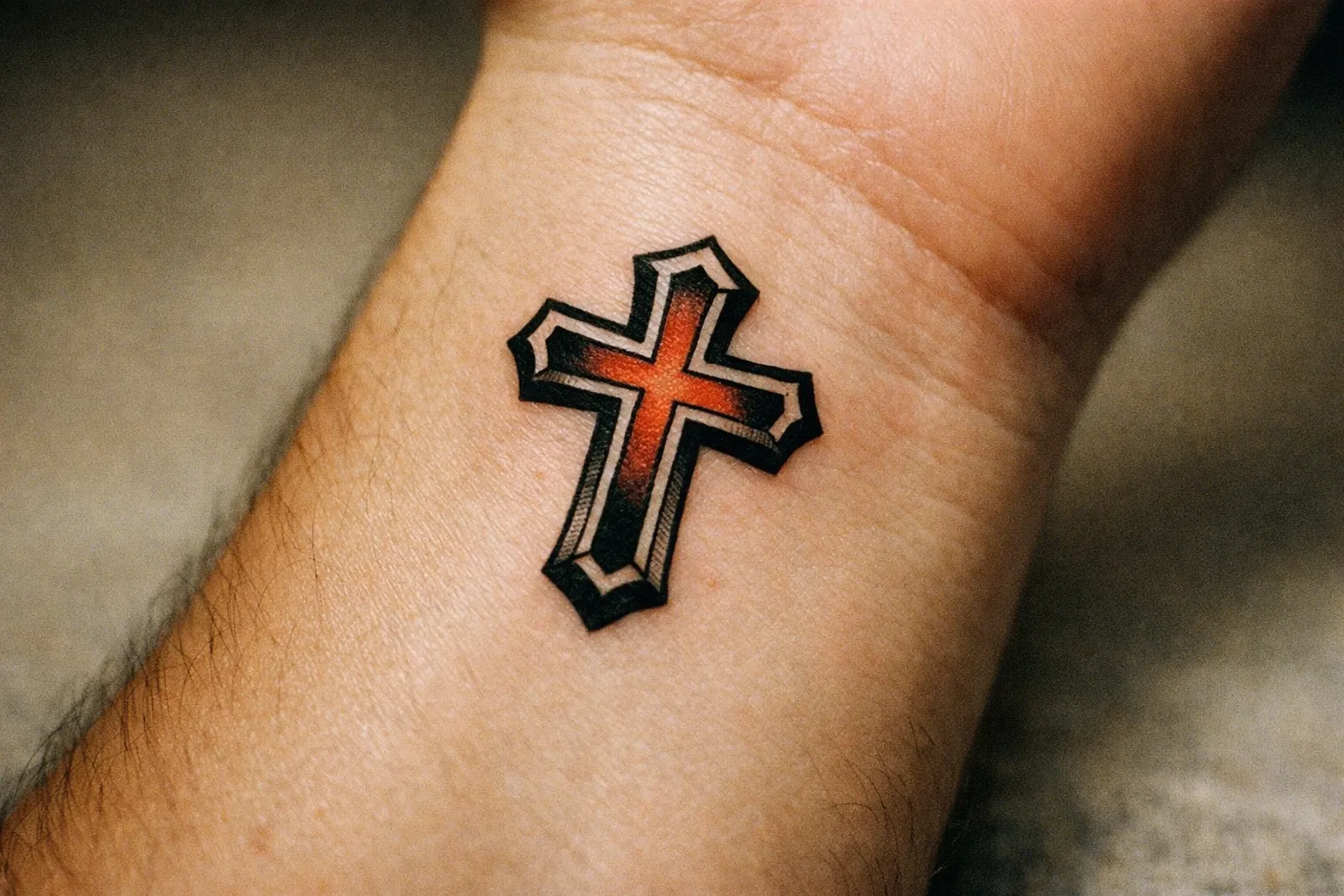 A person's wrist displays a cross tattoo with red and black shading.