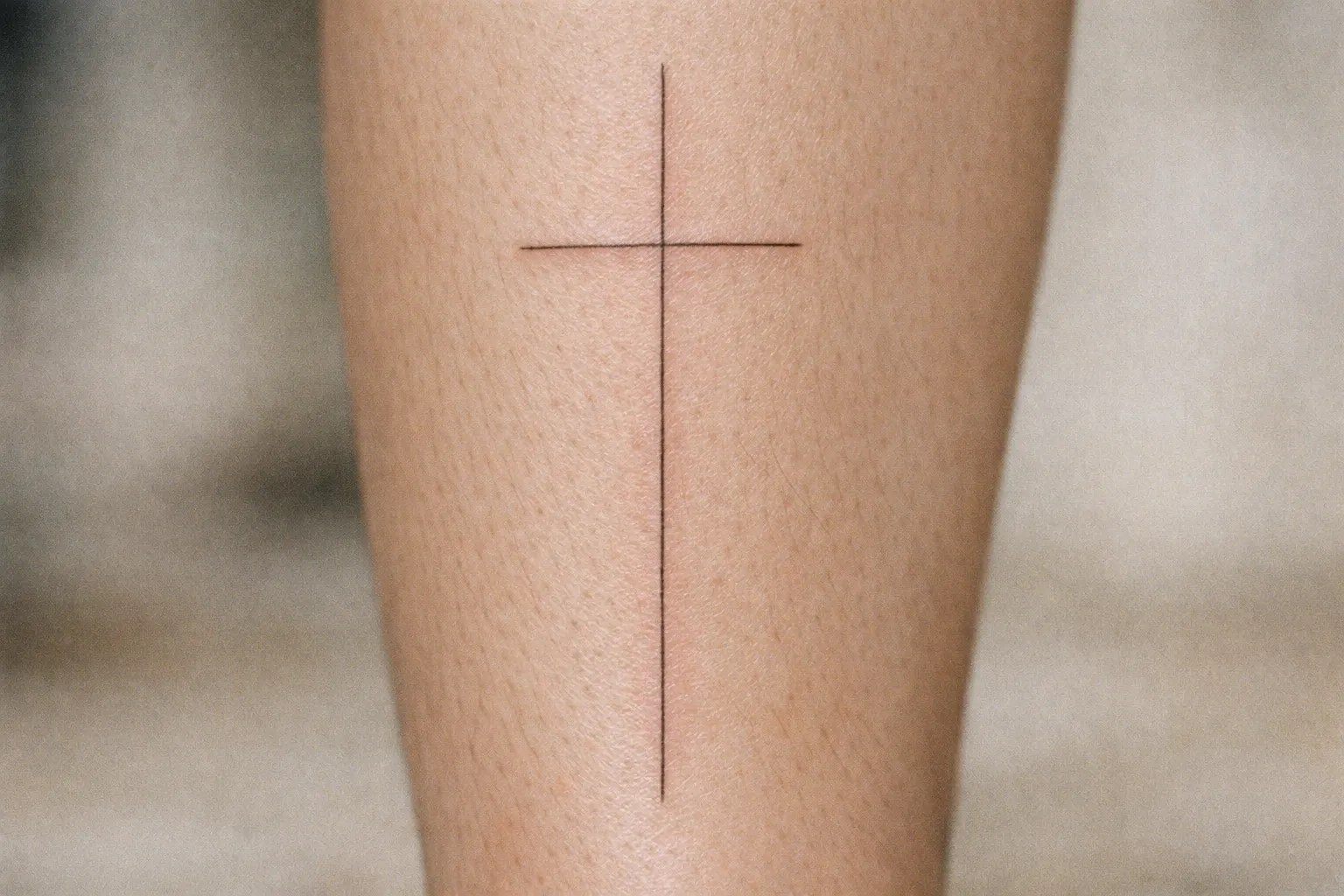 A simple cross tattoo on a person's leg.