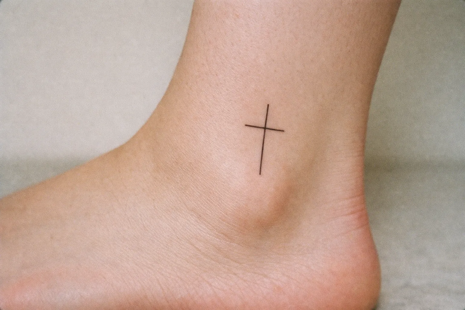 A small cross tattoo on the side of a person's ankle.