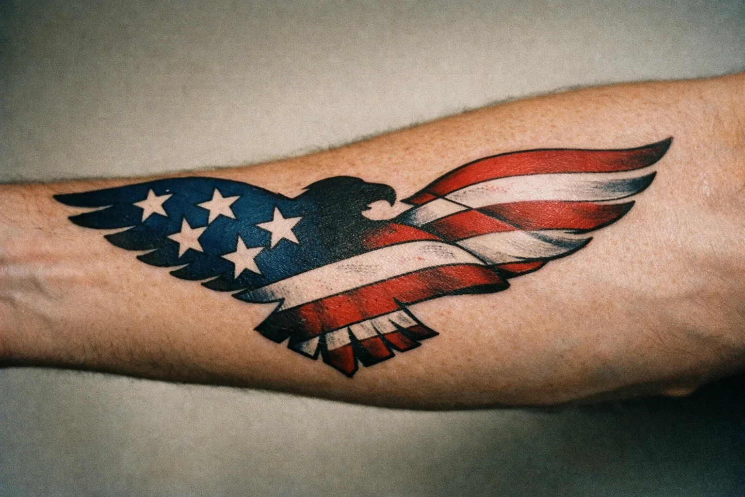 Forearm tattoo that combines an eagle silhouette with an American flag design, integrated across the arm.
