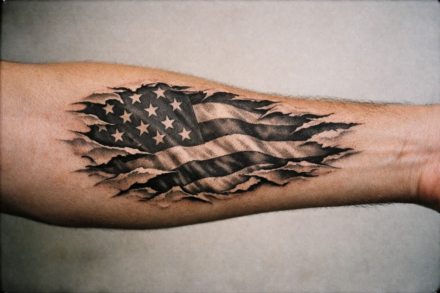 Forearm tattoo of a black-and-grey ripped flag design with torn edges revealing negative space.