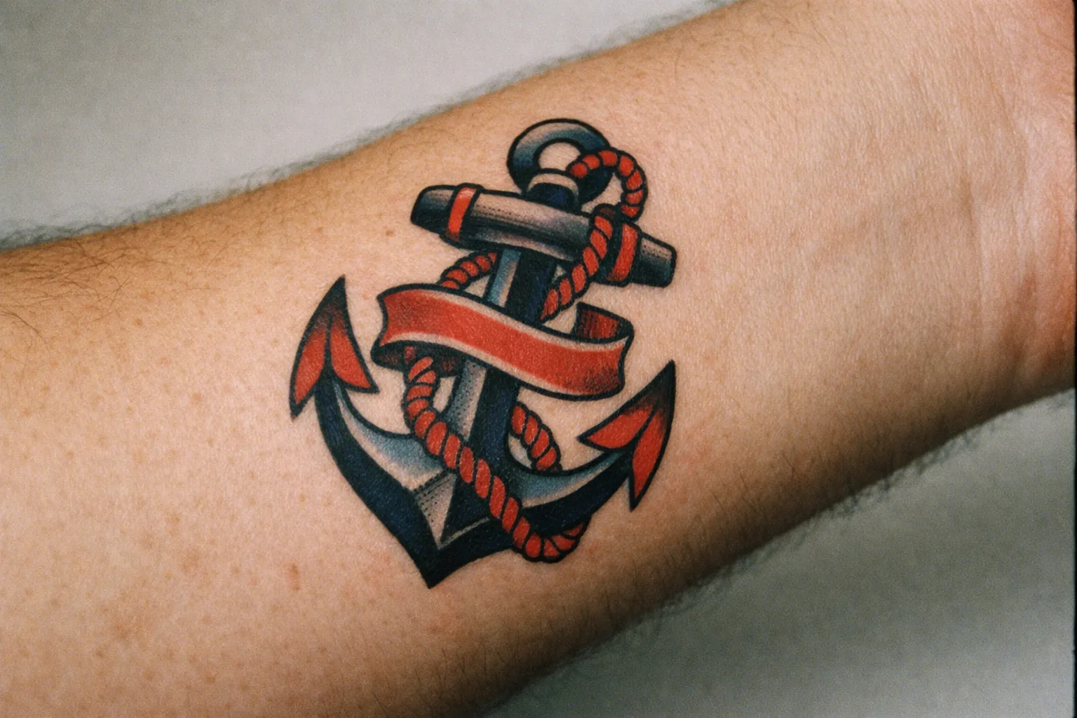 Forearm tattoo showcasing traditional American traditional anchor with bold lines and solid fills