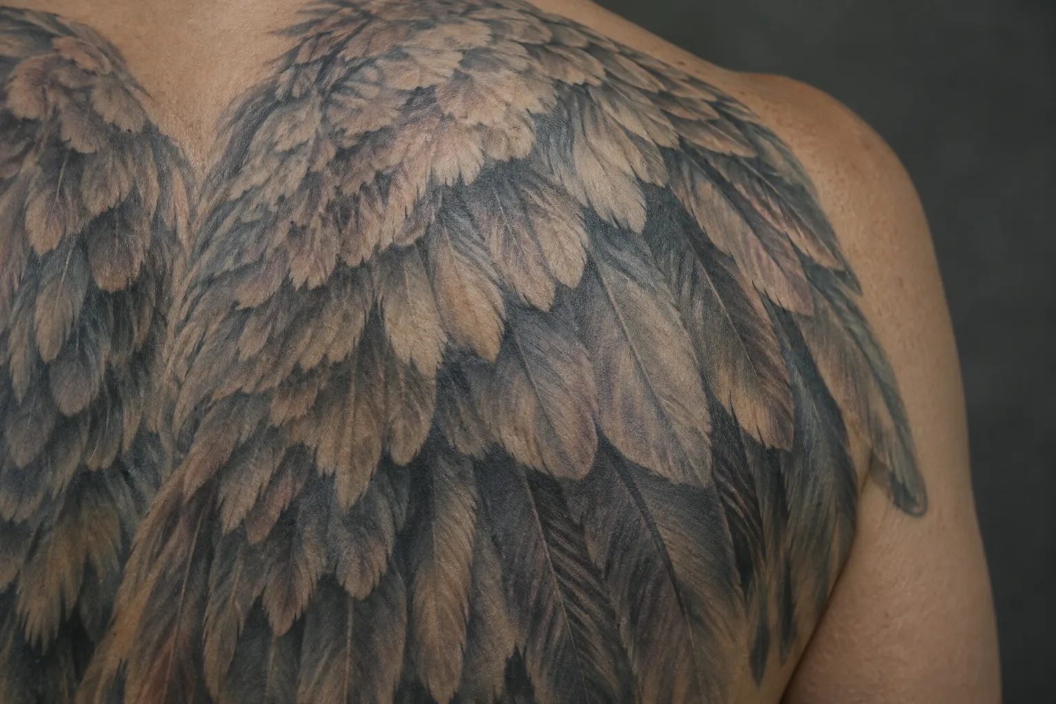 A large feathered angel wing tattoo covers a person's upper back and shoulder.