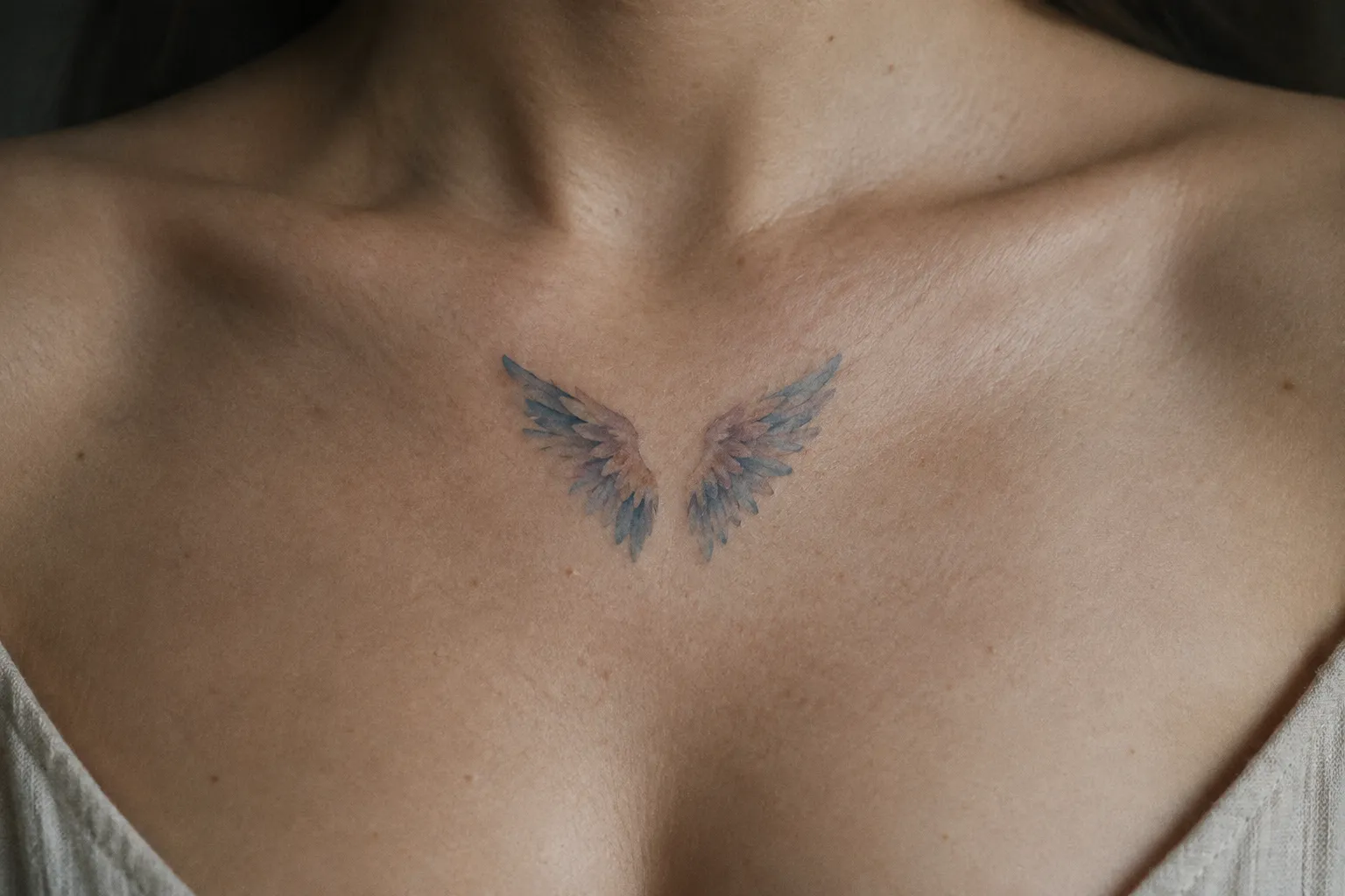 A small pair of angel wings is tattooed at the center of a person's upper chest.