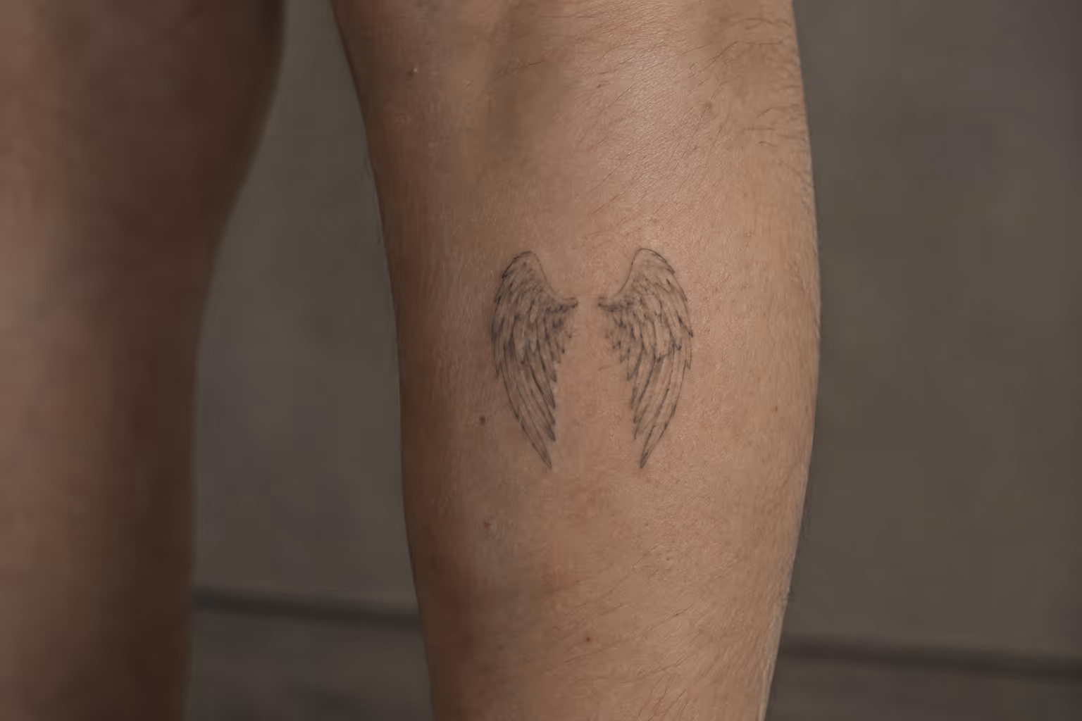 A small fine-line pair of angel wings tattooed on the back of a person's lower leg.