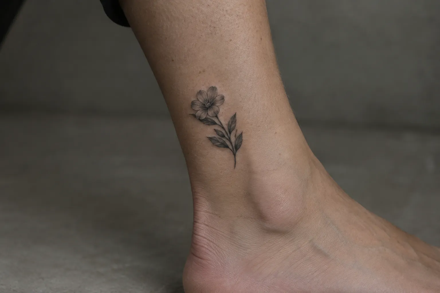 A small flower tattoo sits on the inner ankle above a bare foot.