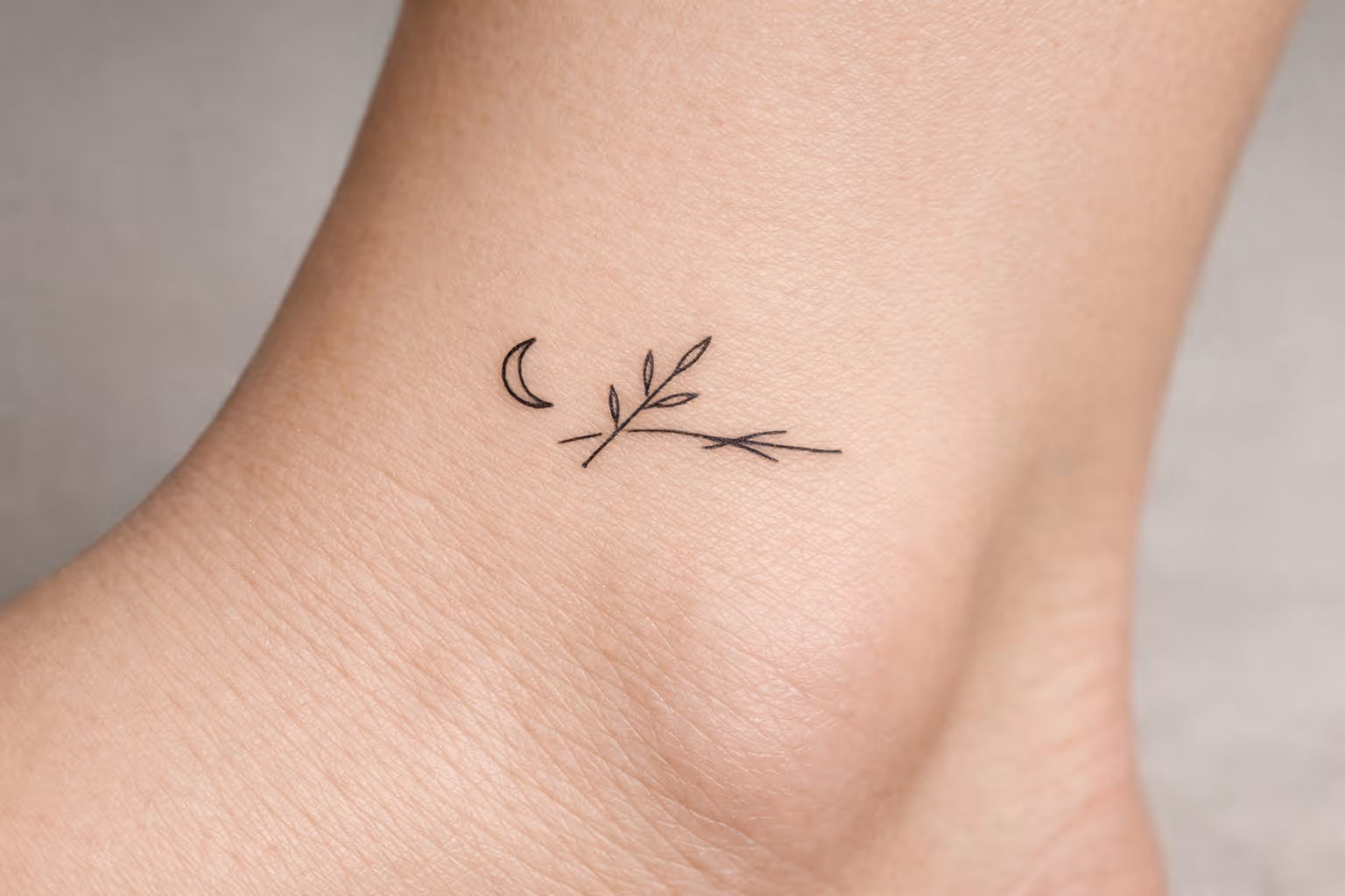 A small moon and branch tattoo on the inside of an ankle.