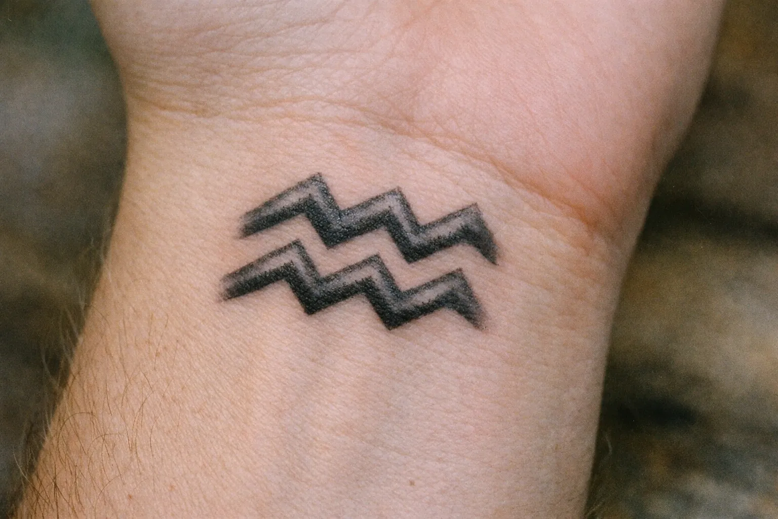 An Aquarius zodiac symbol tattoo on a person's wrist.