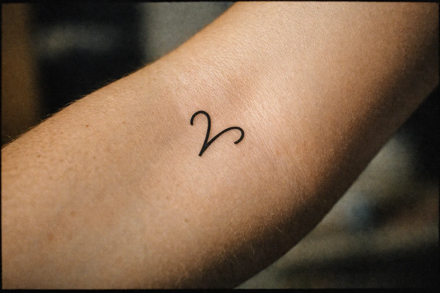 Close-up of a minimalist Aries glyph tattoo on the inner forearm, black ink with clean lines