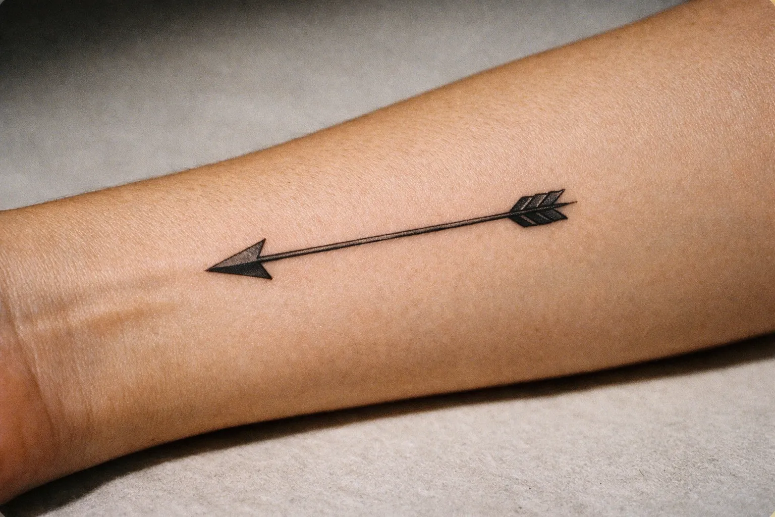 Close-up of a healed black arrow tattoo on forearm; minimalist single-arrow design