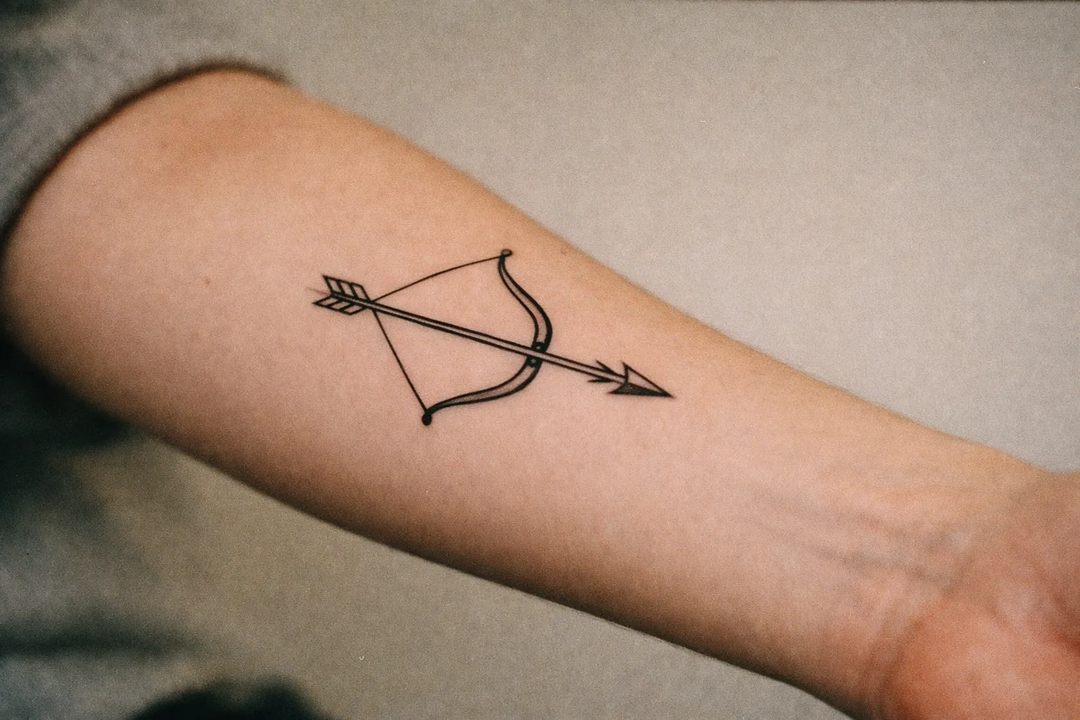 Forearm tattoo of a bow and arrow silhouette in black ink; bold linework