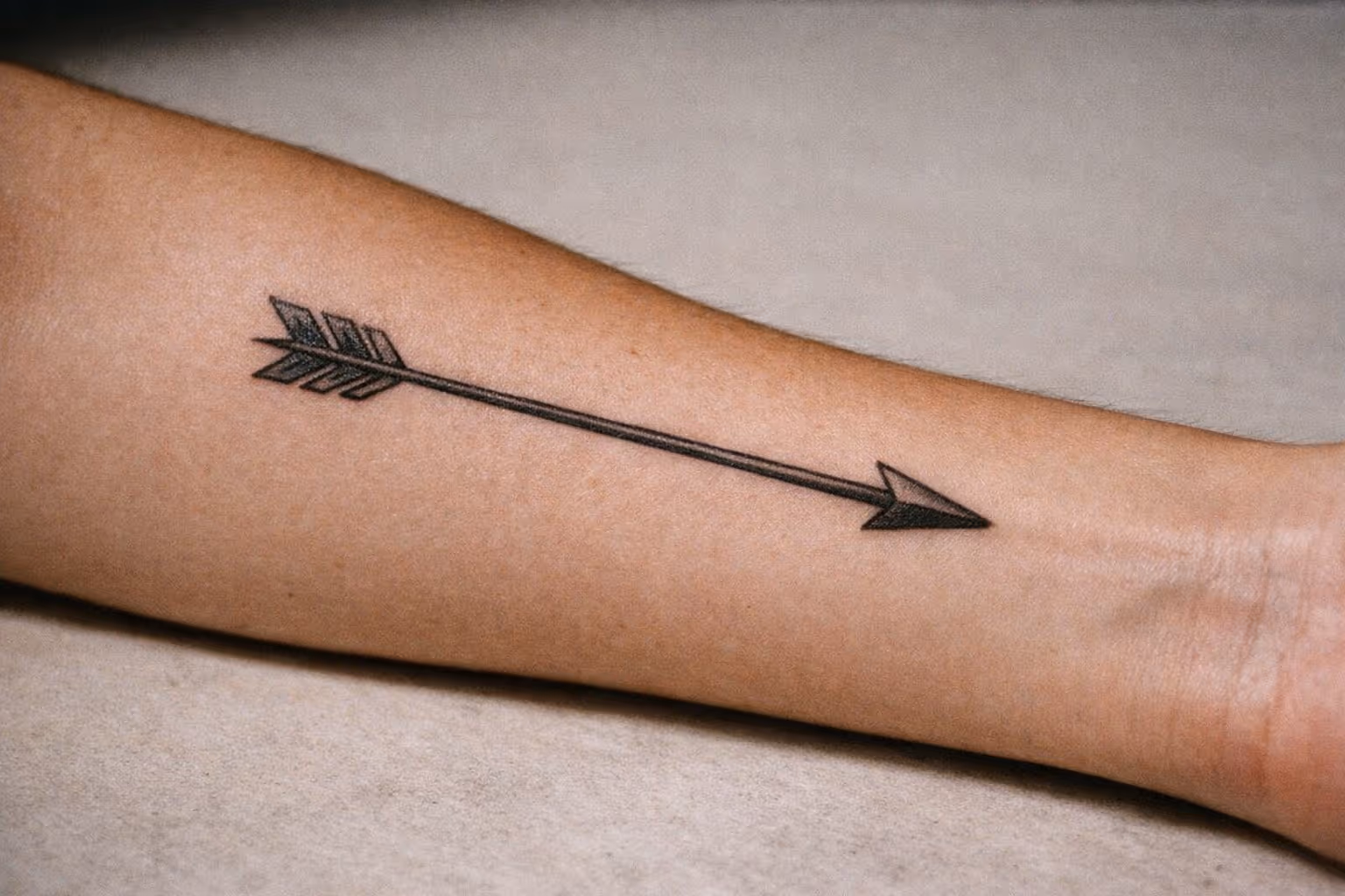 Editorial hero shot of a healed arrow tattoo on forearm, single design with clean linework
