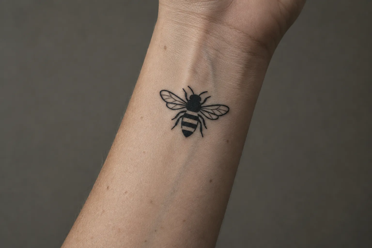 A black bee tattoo sits on the inner wrist.