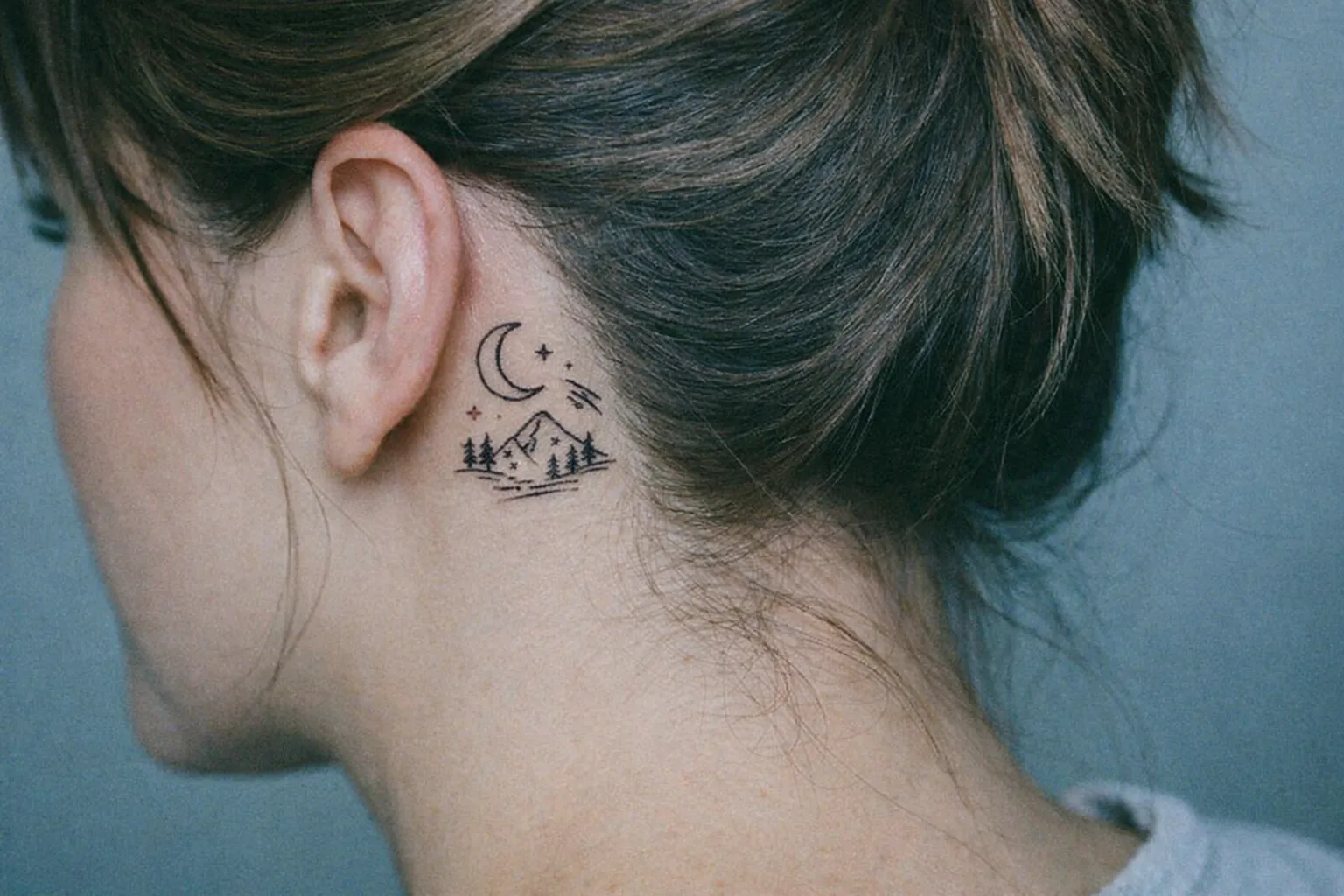A person with a small mountain and moon tattoo behind their ear.