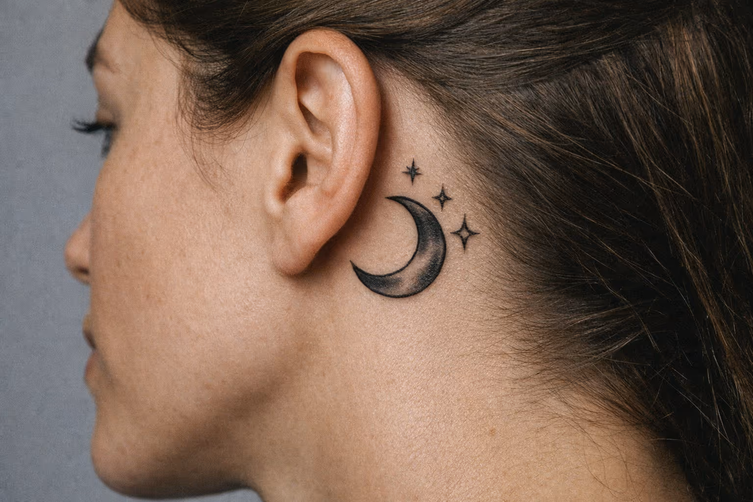 A person with a crescent moon and stars tattooed behind their ear.