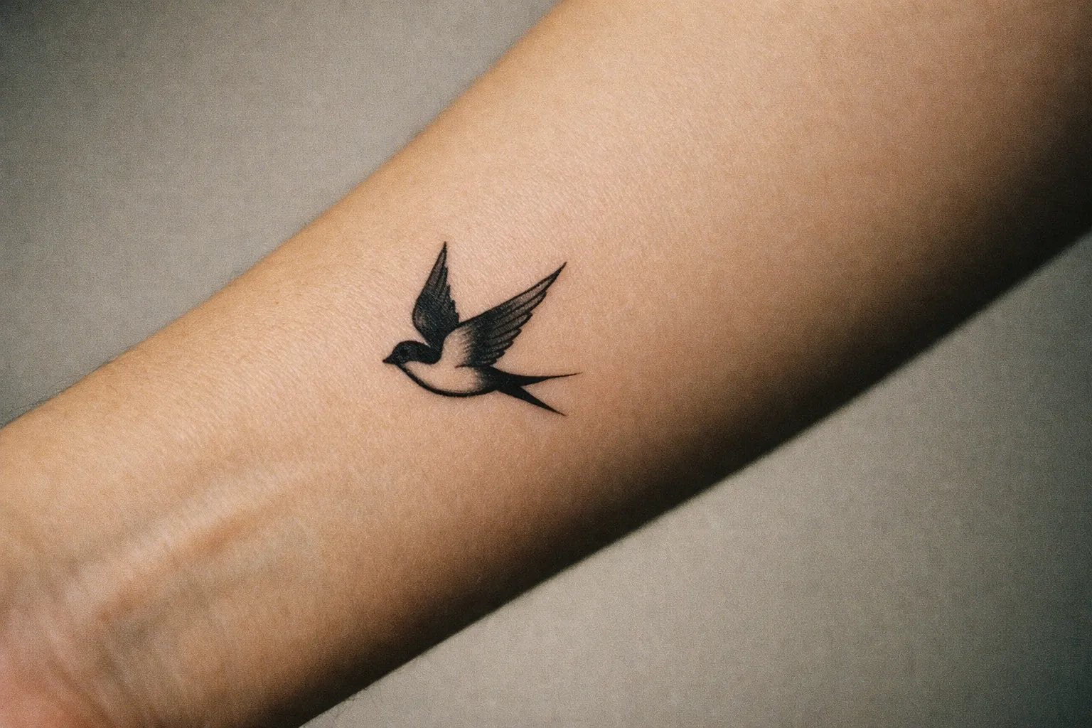 Close-up of a forearm with a small, minimalist swallow tattoo in black ink