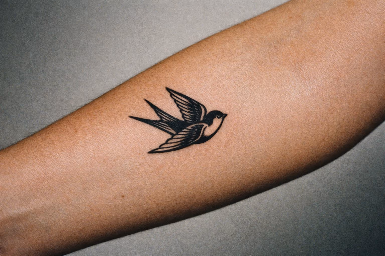 Editorial close-up of a forearm with a small swallow tattoo in black ink