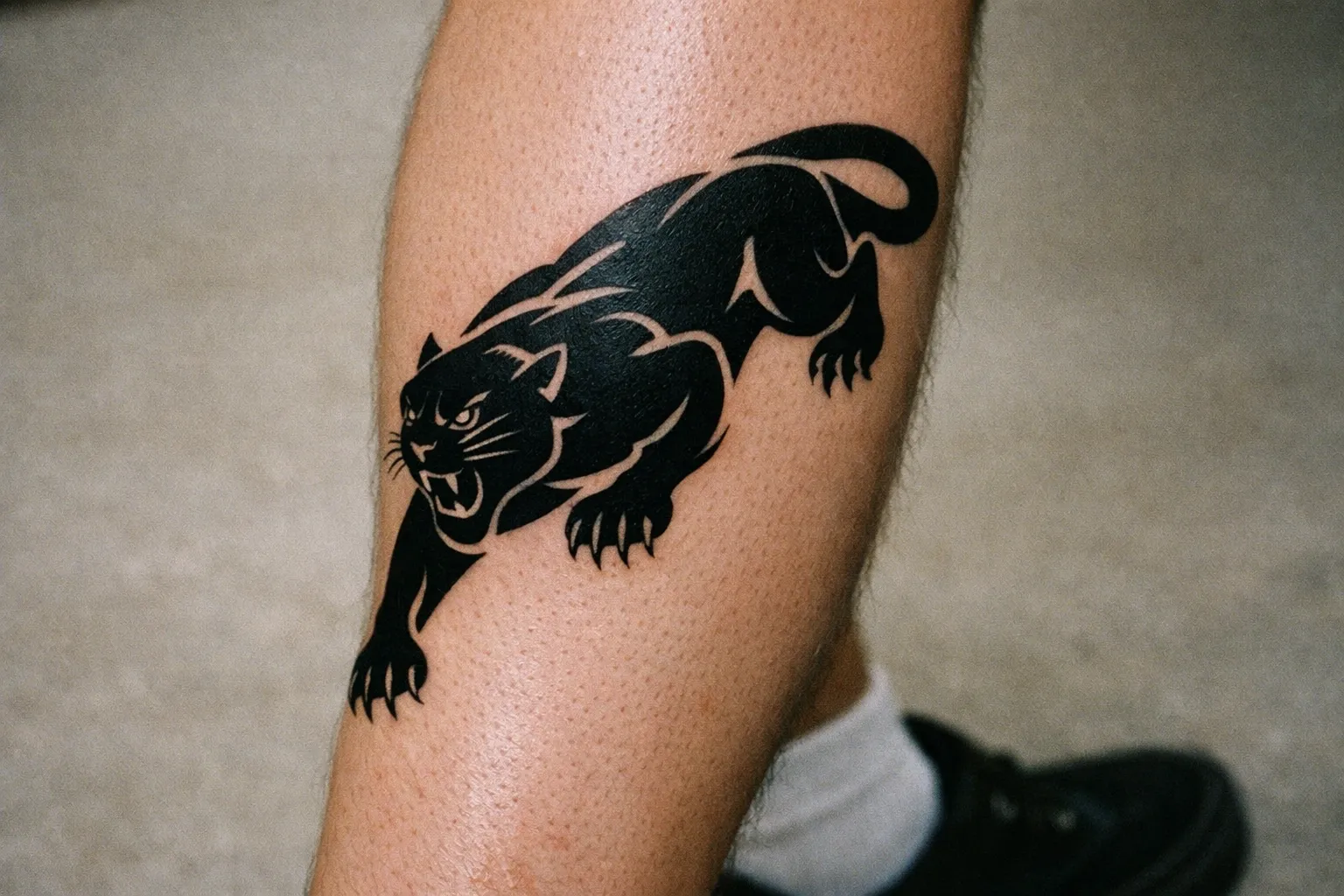 Calf tattoo of a Black Panther in mid-stride symbolizing resilience