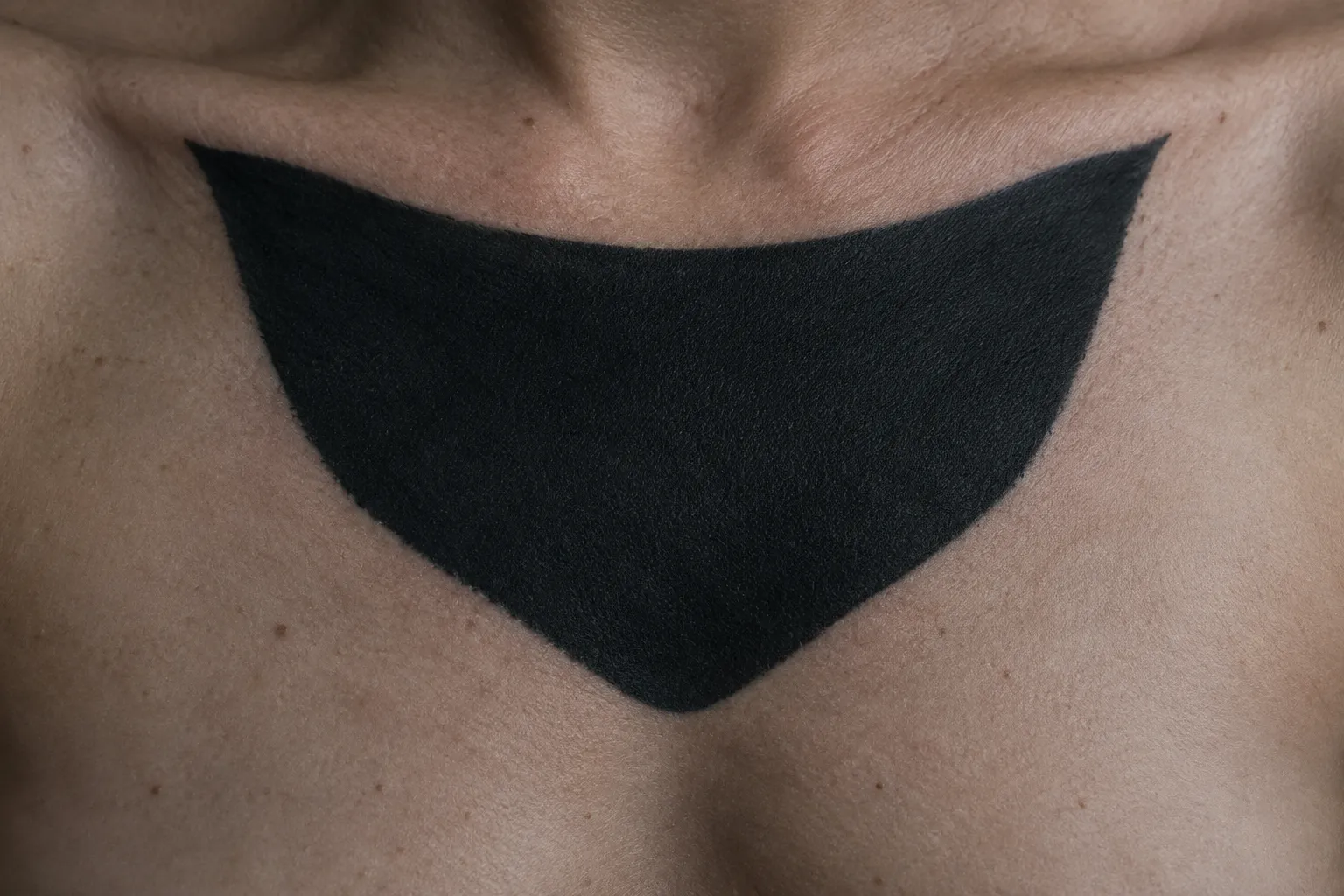 A person's chest bears a large solid black blackout tattoo.