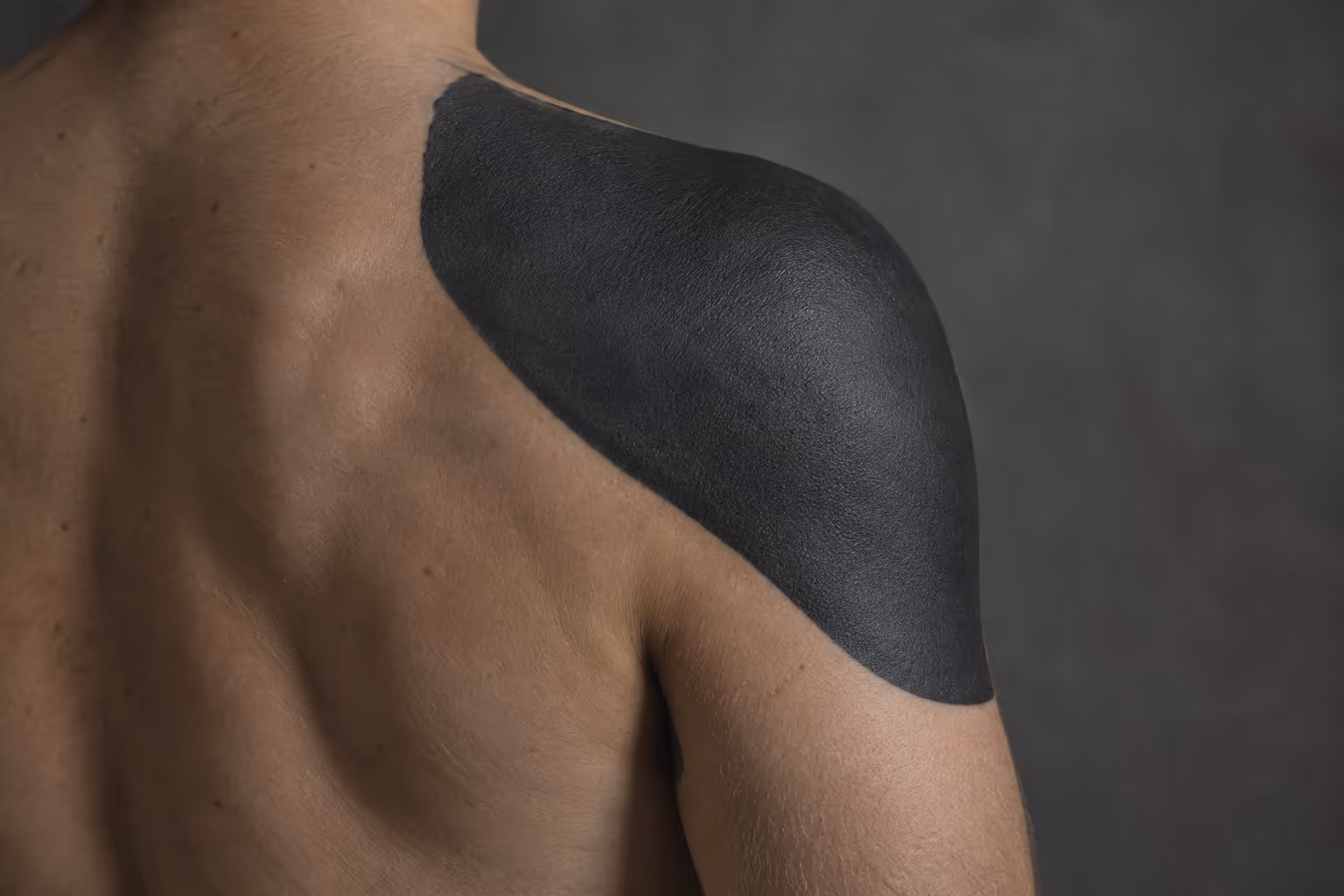 A person's shoulder and upper arm feature a solid black blackout tattoo.
