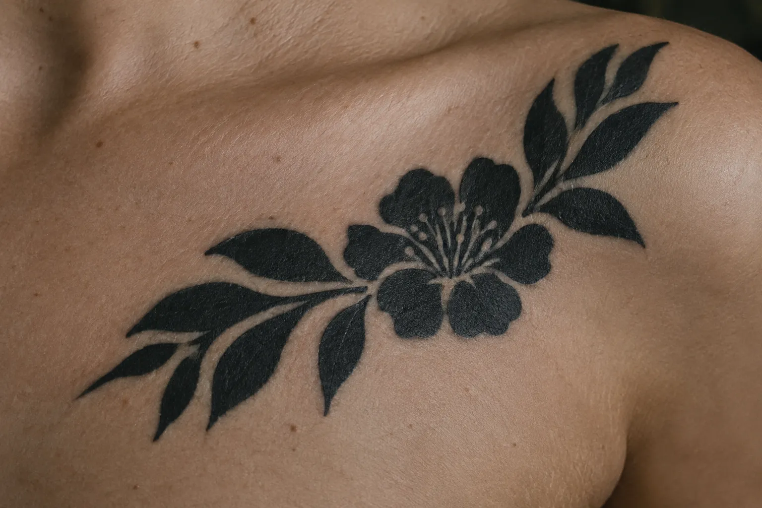 A solid black floral tattoo stretches across a person's upper chest and shoulder.