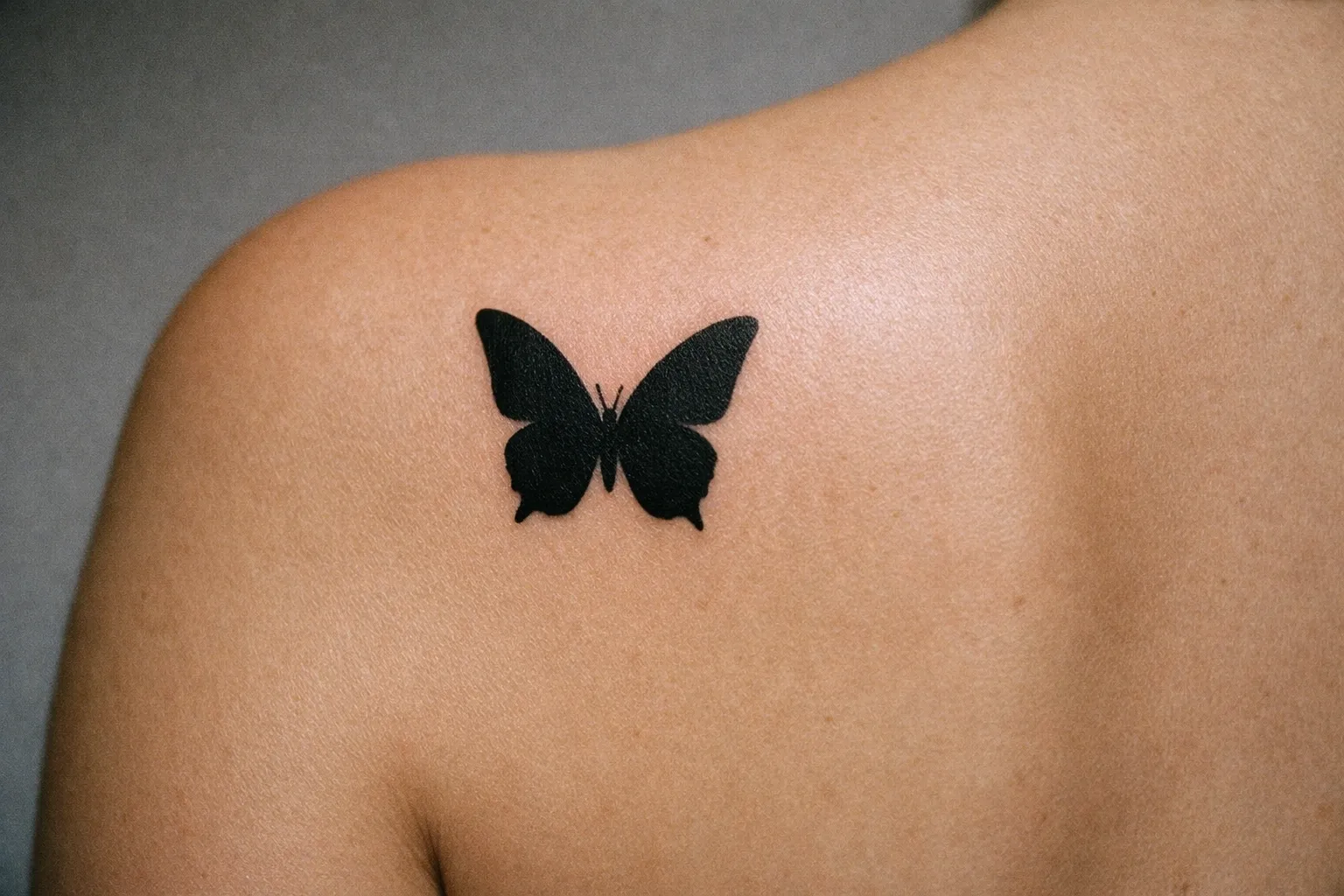 A black butterfly tattoo on a person's upper back near the shoulder blade.