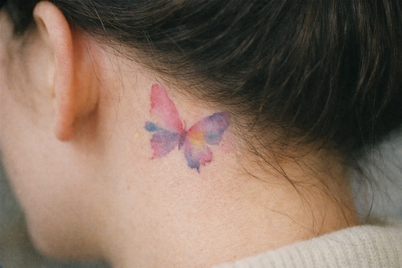 A colorful butterfly tattoo on the side of a person's neck, just below the hairline.