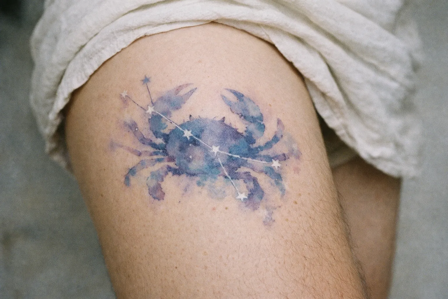A watercolor-style crab and constellation tattoo on a person's upper thigh.