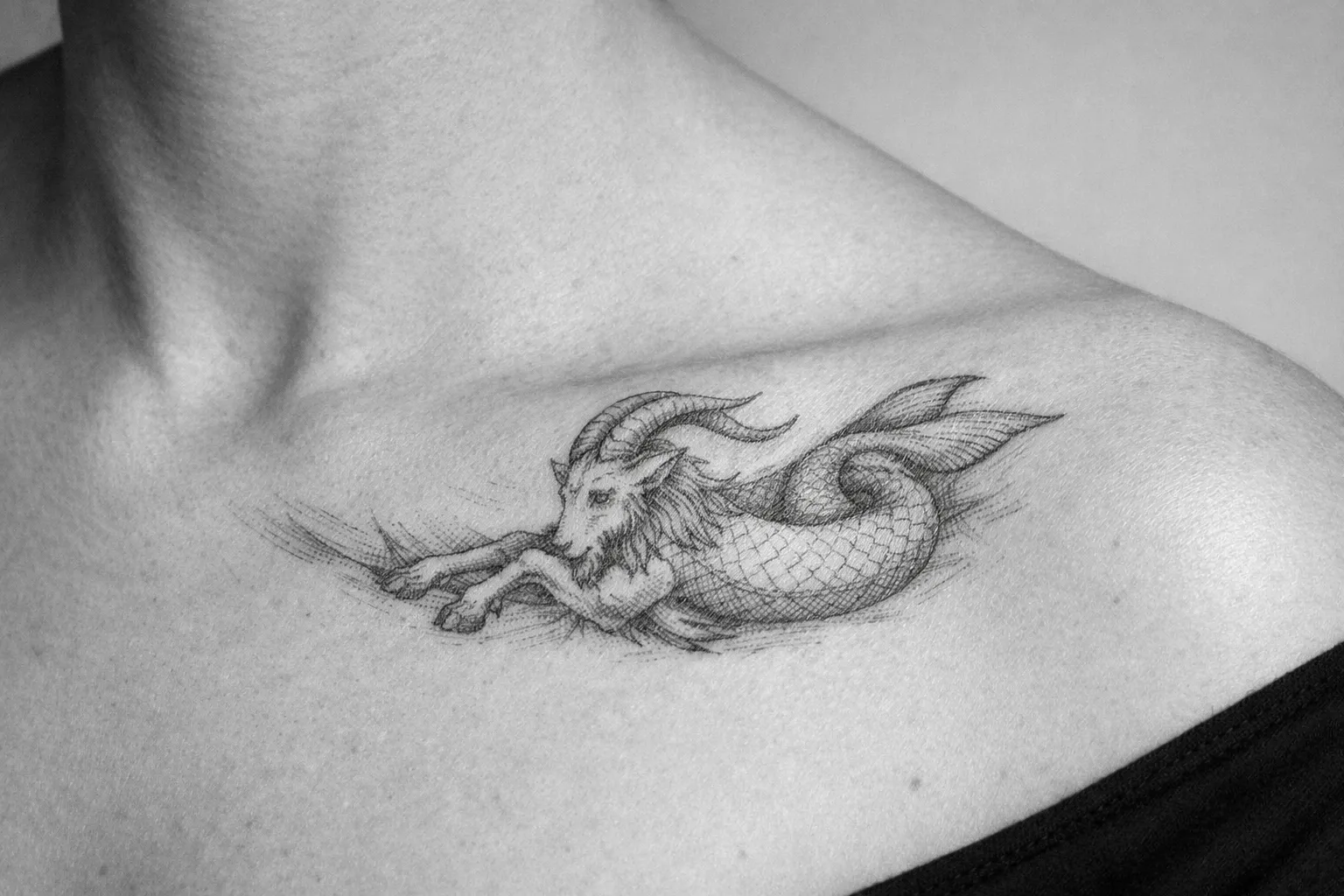 A Capricorn sea-goat tattoo is inked on a person's upper chest near the collarbone.