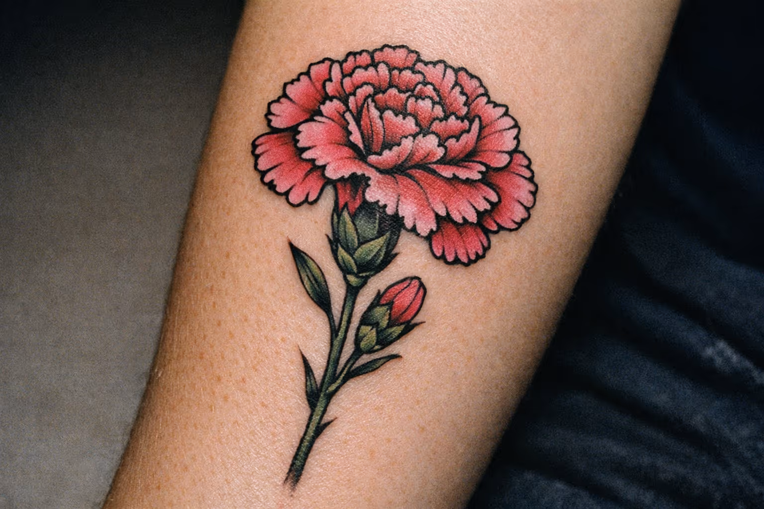 Editorial feature image: close-up of a vibrant carnation tattoo on forearm, showing crisp linework and rich color