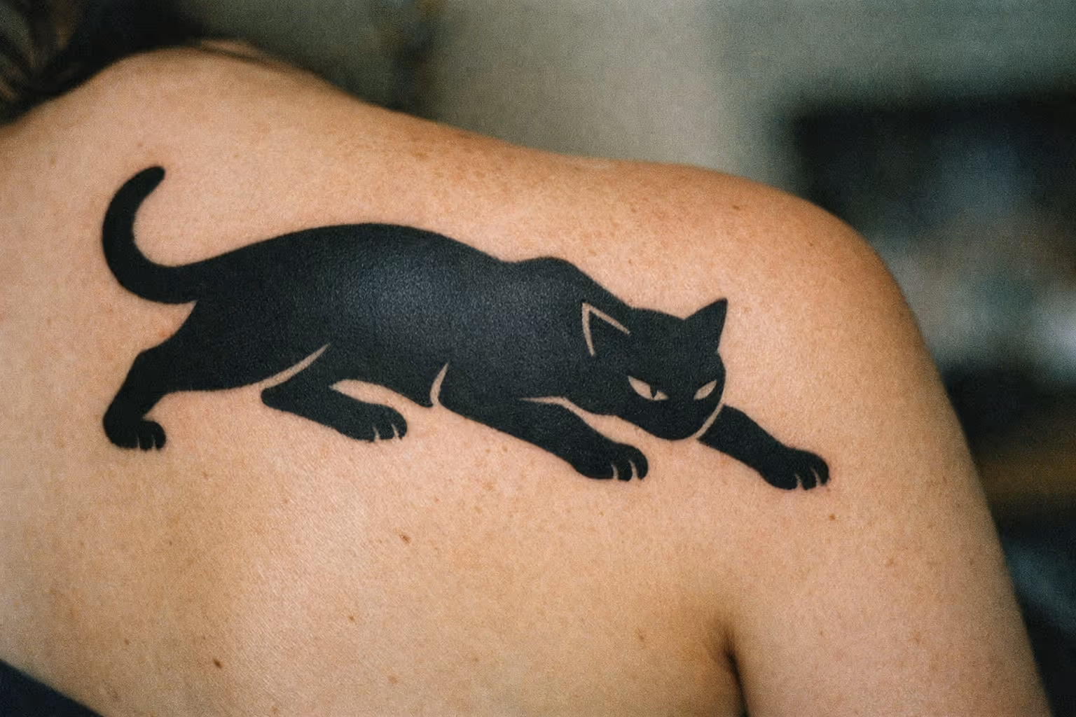 A black cat tattoo on a person's upper back and shoulder.