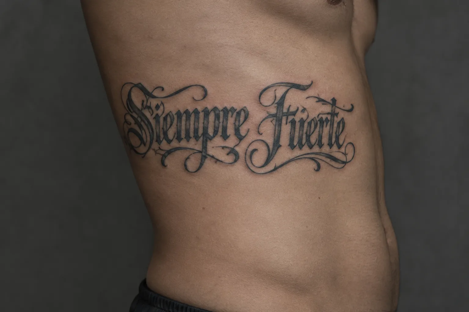 A blackletter 'Siempre Fuerte' tattoo spans a person's side torso.