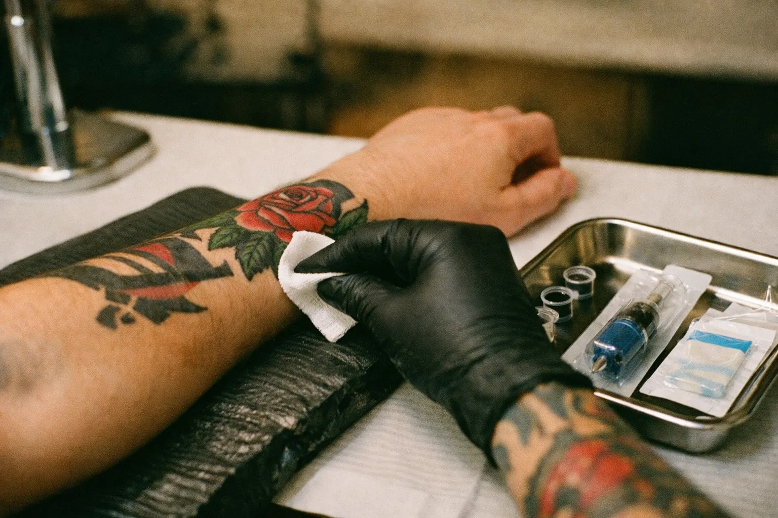 Forearm tattoo with a laptop screen softly blurred in the background showing designs