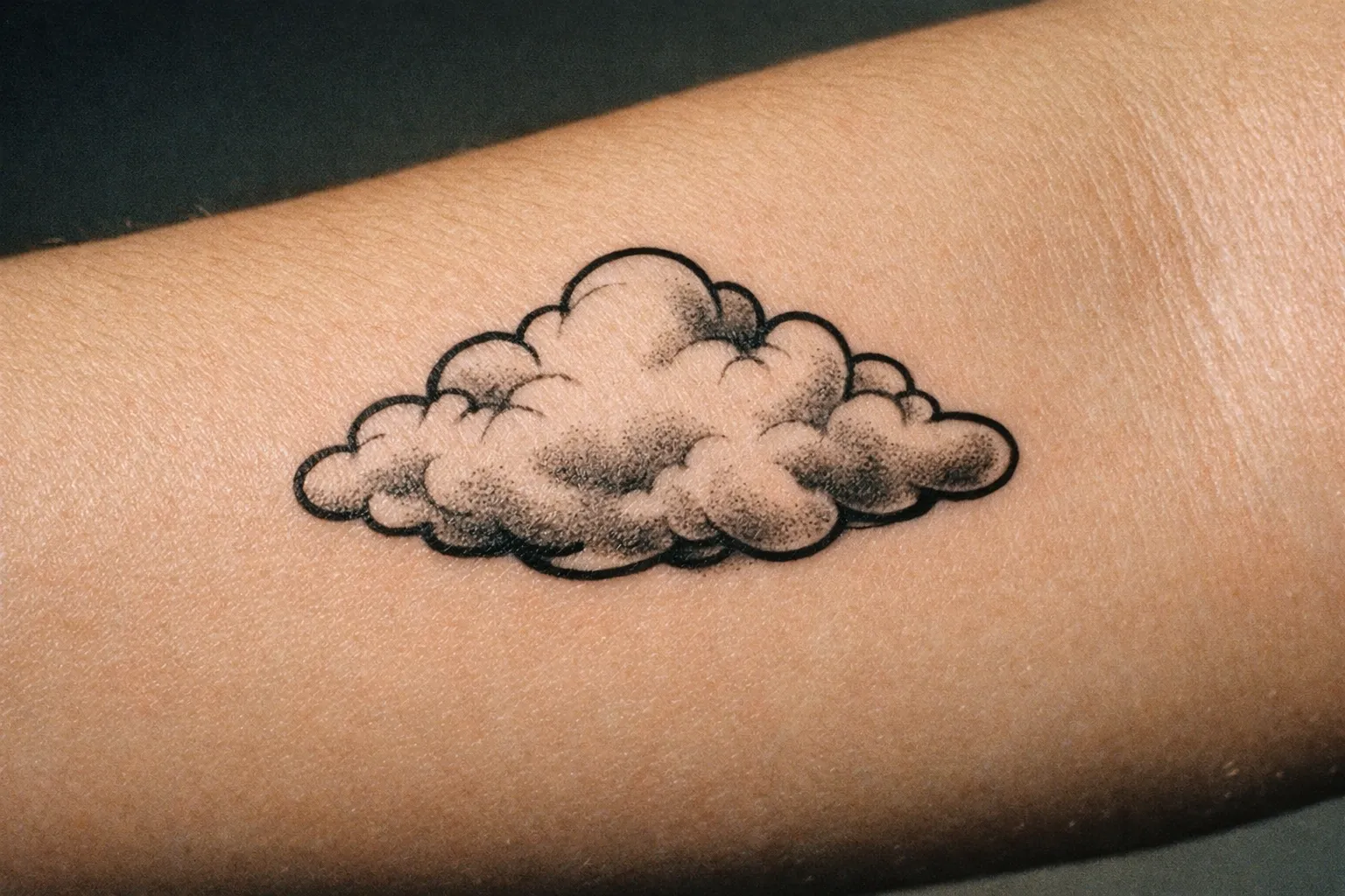 Forearm close-up of a cloud tattoo with soft shading