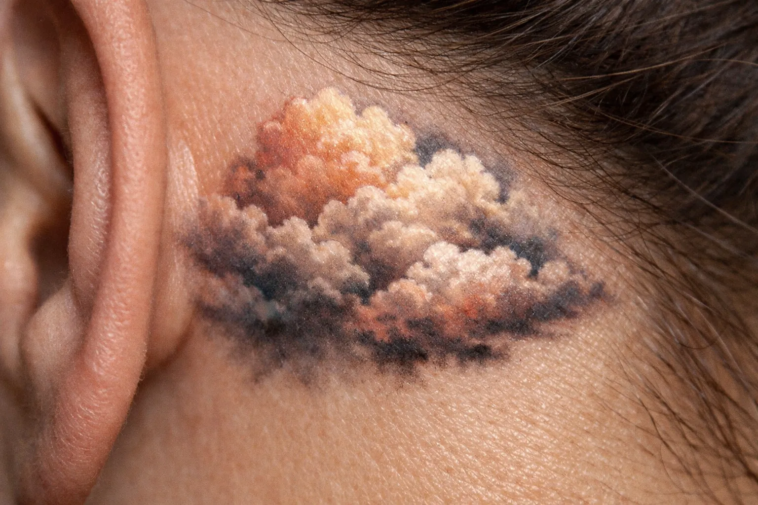 A detailed cloud tattoo is inked on the skin just above a person's ear.