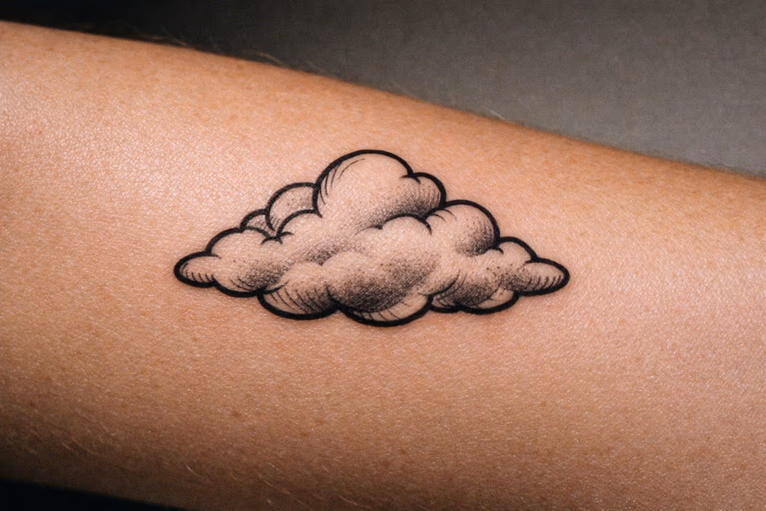 Editorial close-up of a cloud tattoo on forearm, single bold cloud