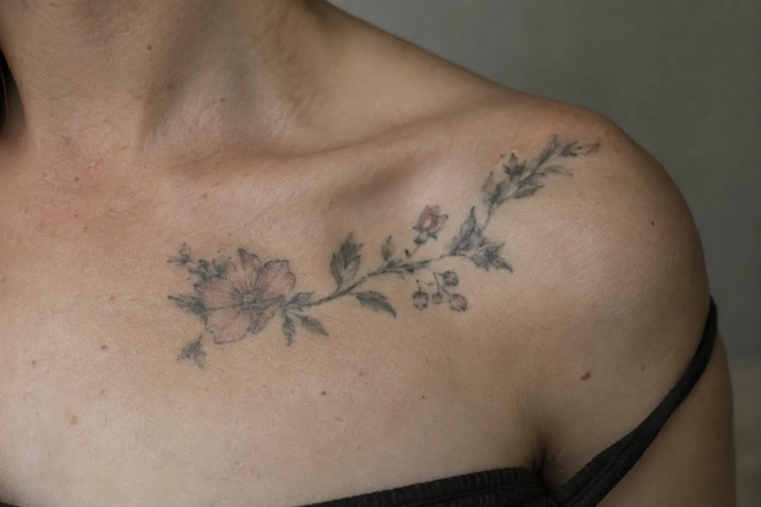 A floral tattoo follows a person's collarbone and shoulder.