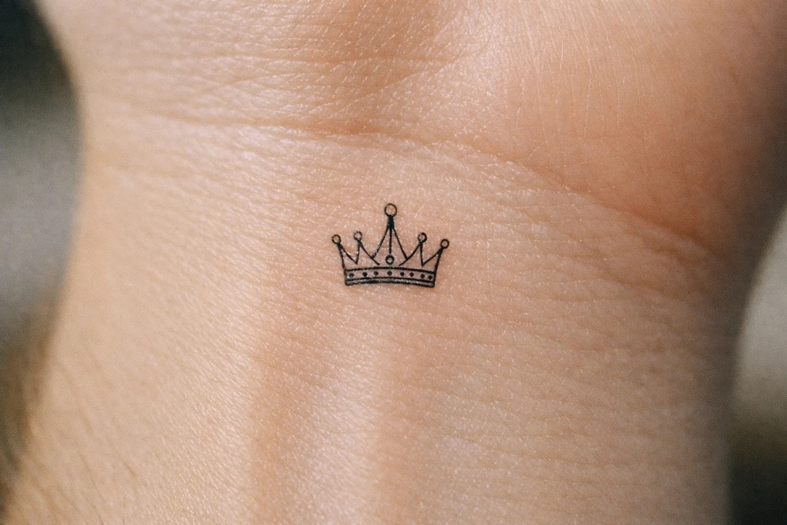 Macro view of a tiny crown tattoo on inner wrist showing fine linework