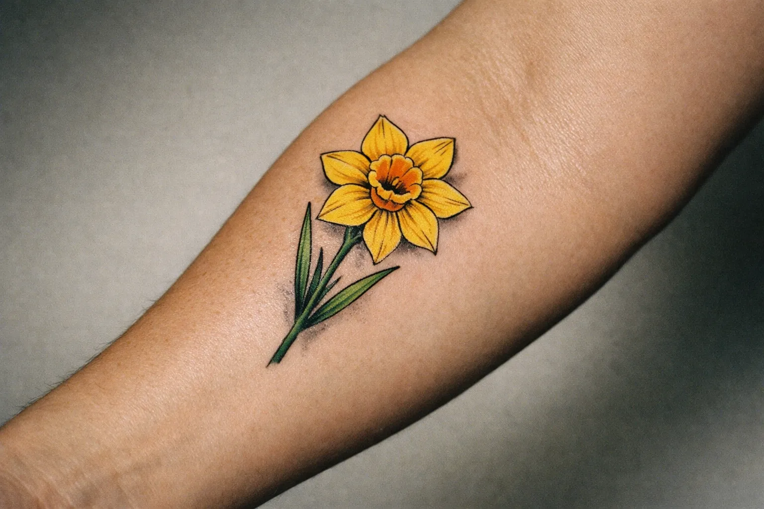 Close-up of a forearm with a daffodil tattoo showing bold black linework and yellow petals