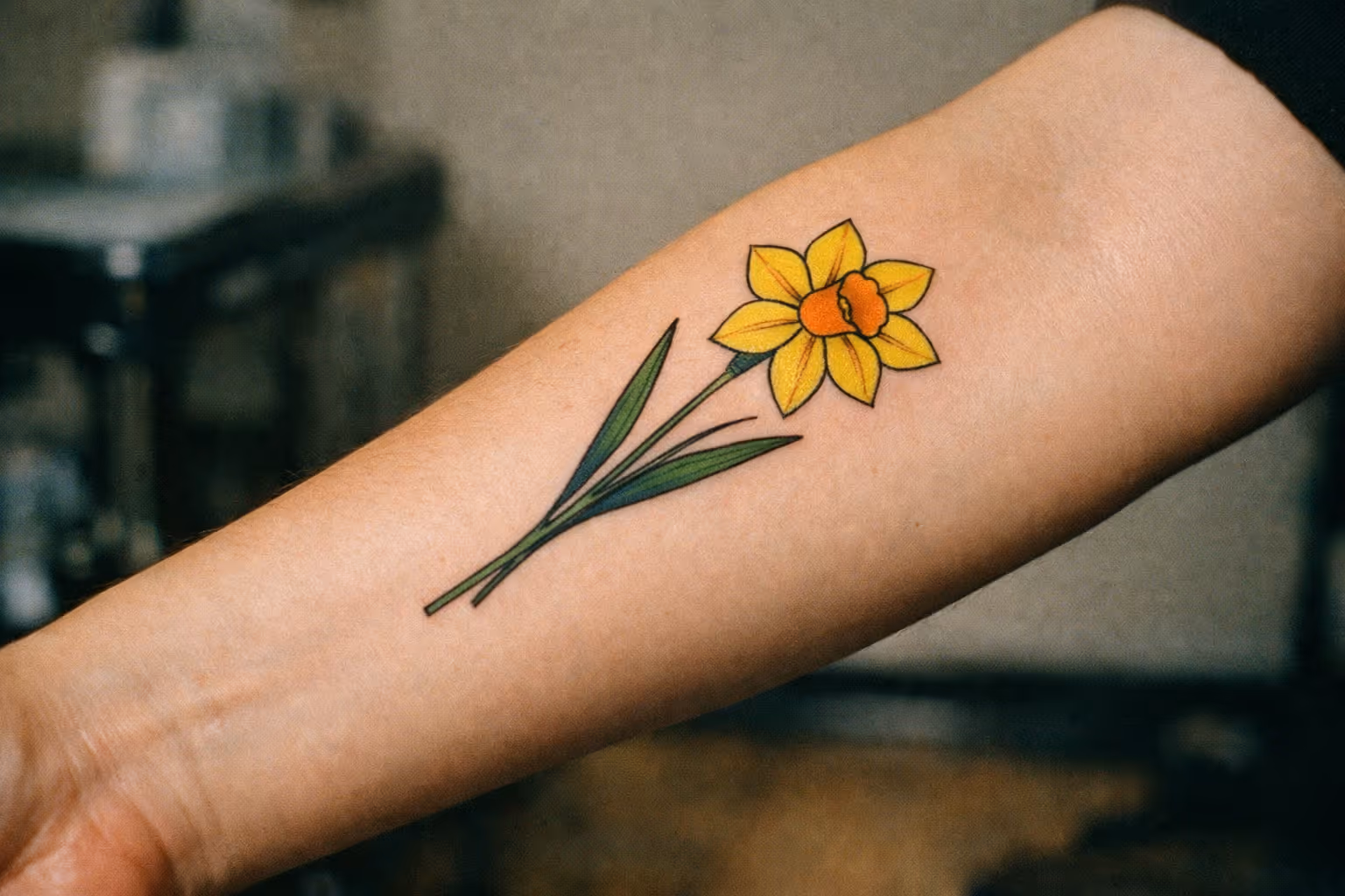 Hero shot: close-up of a healed daffodil tattoo on a forearm in editorial lighting