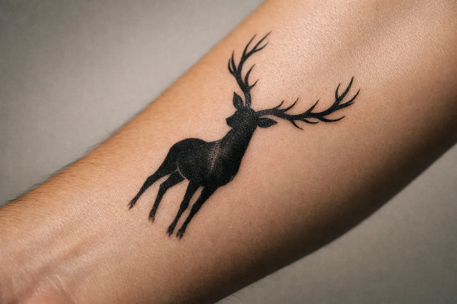 Black-ink deer silhouette tattoo on forearm, macro close-up