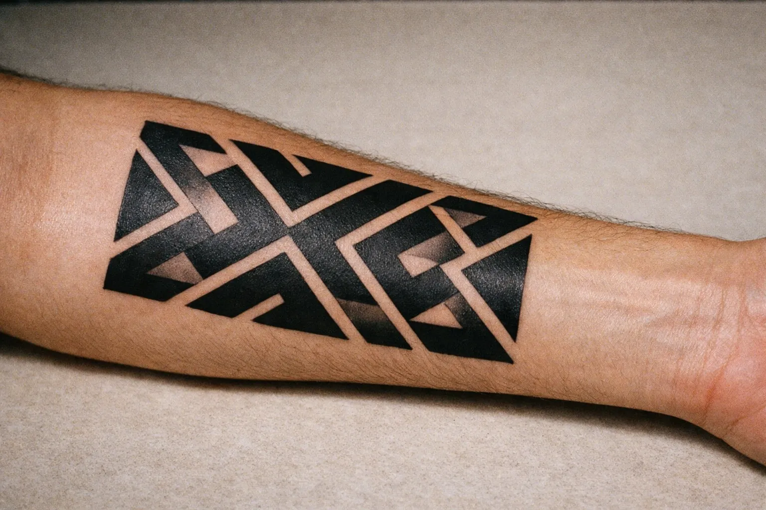 Inner forearm close-up of a bold geometric tattoo with interlocking lines and negative space