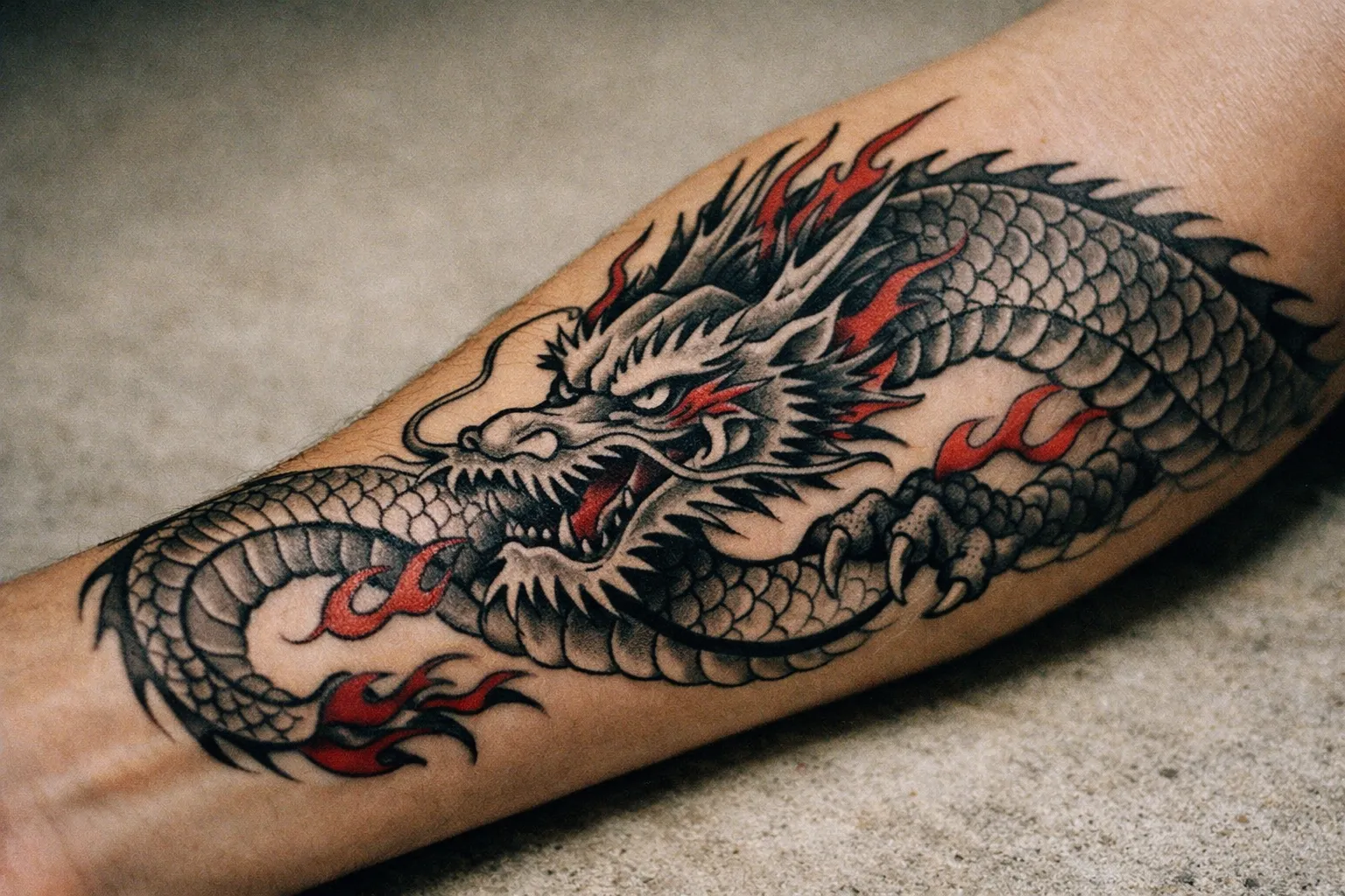 Forearm tattoo close-up of a traditional Japanese-inspired dragon with bold black lines and red accents