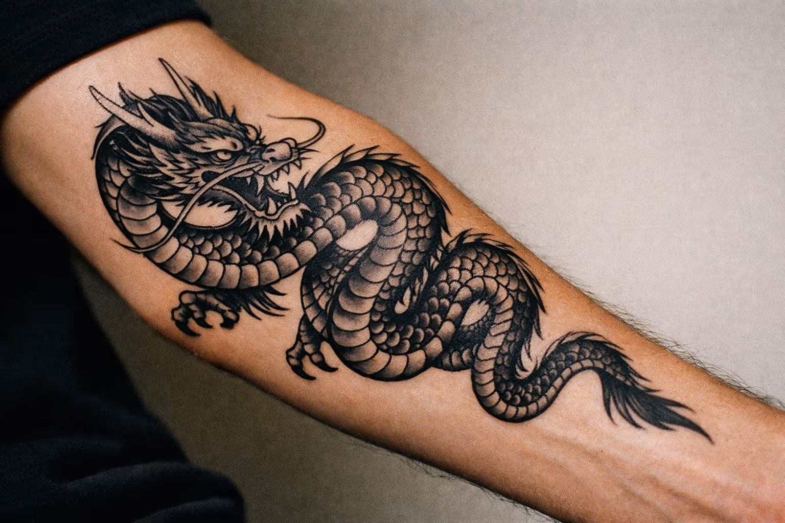 Editorial close-up of a forearm dragon tattoo in black-and-gray style, showing bold linework and subtle shading