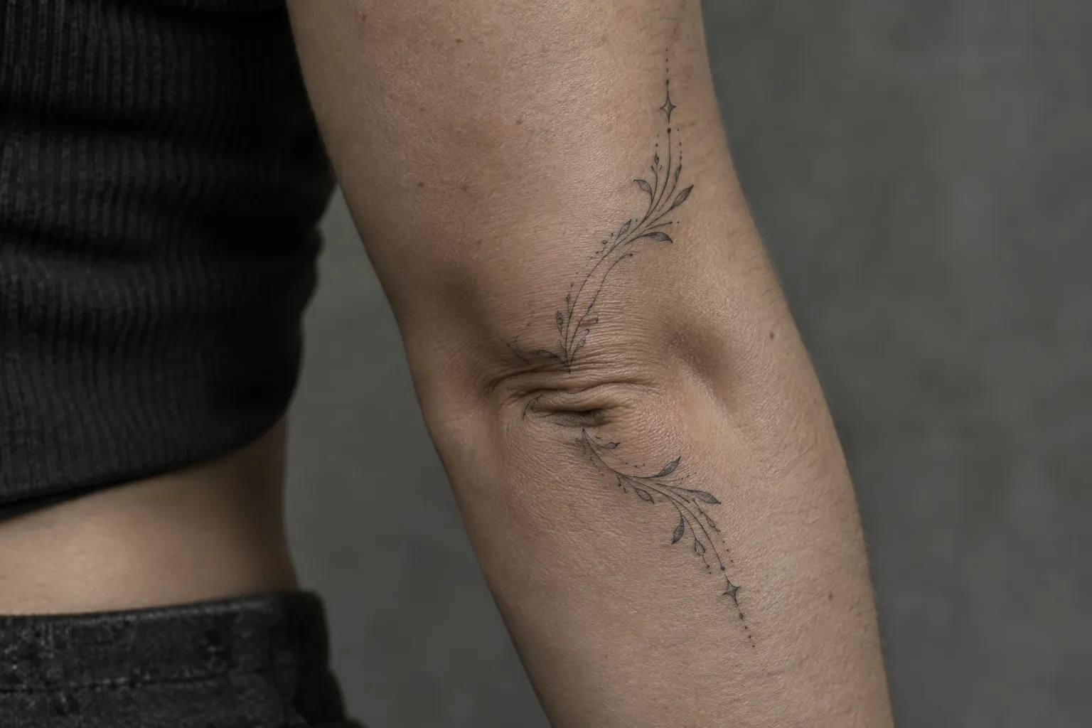 A person has a delicate botanical tattoo curving across the inner elbow.